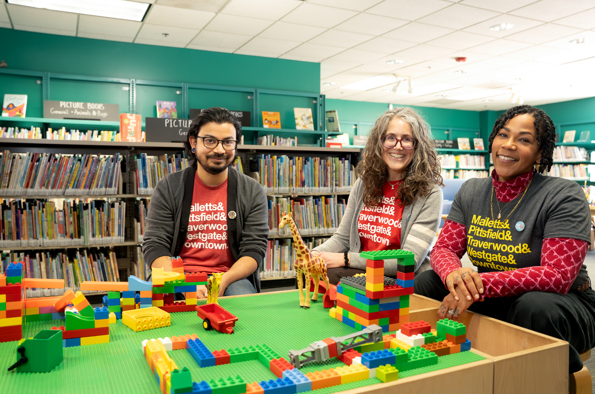 Candidates Gaurav Kulkarni, Rachel Goldberg and Cassie Haynes, wearing AADL Summer Game shirts and sitting in the childrens section of the downtown library.